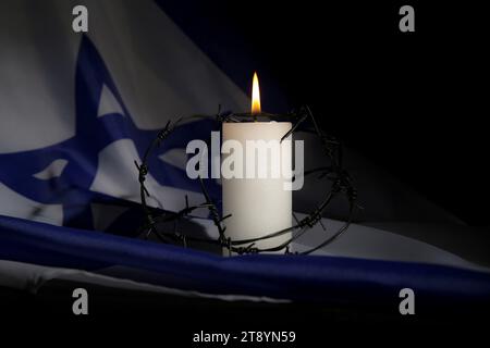 Brennende Kerze mit Stacheldraht auf der Flagge Israels, Nahaufnahme. Internationaler Holocaust-Gedenktag Stockfoto