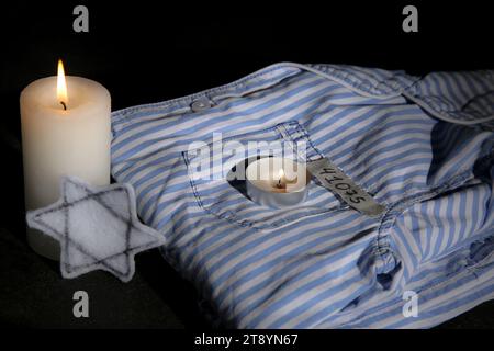 Brennende Kerzen mit jüdischem Abzeichen und Gefangenenuniform auf dunklem Hintergrund. Internationaler Holocaust-Gedenktag Stockfoto