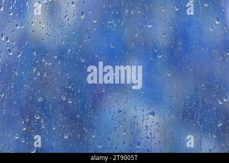 Regentropfen auf dem Fensterglas. Unscharfer farbiger Hintergrund außerhalb des Fensters Stockfoto