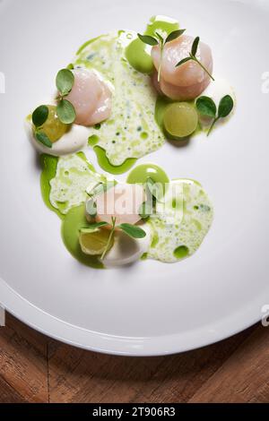 Jakobsmuscheln auf einem großen runden weißen Teller auf einem Holztisch, das Gericht eines großartigen Küchenchefs. Stockfoto