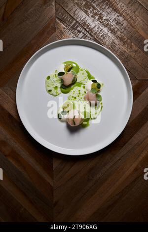 Jakobsmuscheln auf einem großen runden weißen Teller auf einem Holztisch, das Gericht eines großartigen Küchenchefs. Stockfoto