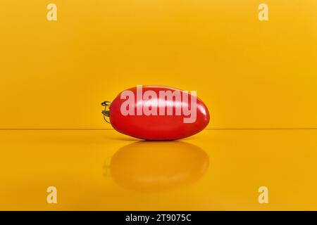 Ganze rote italienische Tomate auf gelbem Hintergrund, Vorderansicht mit Reflexion Stockfoto