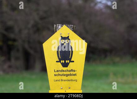 Stahnsdorf, Deutschland. November 2023. Ein Schild neben einer Wiese und einem Wald zeigt einen schwarzen Uhu auf gelbem Hintergrund als Zeichen für ein Landschaftsschutzgebiet. Quelle: Soeren Stache/dpa/Alamy Live News Stockfoto