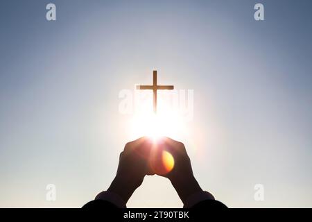 Hell leuchtendes Sonnenlicht und Silhouette christlicher Hände, die das Kreuz Jesu Christi hoch halten, das Tod und Auferstehung symbolisiert Stockfoto