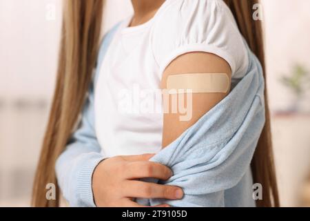 Mädchen mit klebendem Pflaster am Arm nach der Impfung drinnen, Nahaufnahme Stockfoto