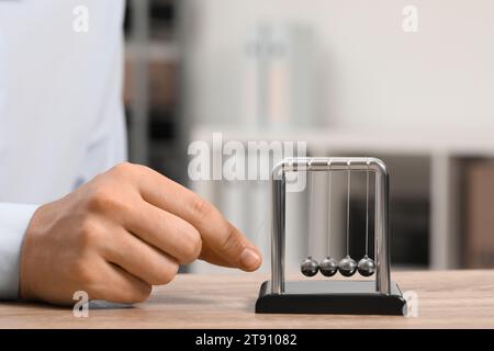 Mann, der mit Newtons Wiege am Tisch spielt, Nahaufnahme. Physikalisches Gesetz der Energieeinsparung Stockfoto