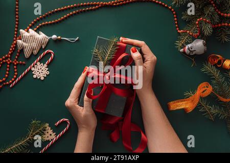 Hände liegen auf Geschenk in grüner Verpackung auf grünem Hintergrund mit Weihnachtsbaumdekorationen Stockfoto