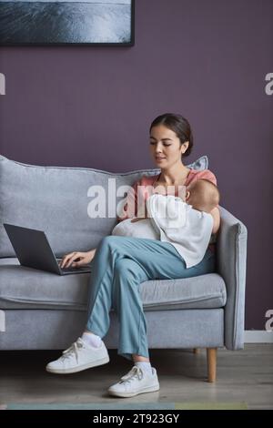 Porträt einer jungen Mutter, die das Baby hält und einen Laptop benutzt, während sie im Mutterschaftsurlaub von zu Hause aus arbeitet Stockfoto