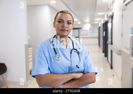 Porträt einer glücklichen birassischen Ärztin mit Peelings und Stethoskop im Spitalflur Stockfoto