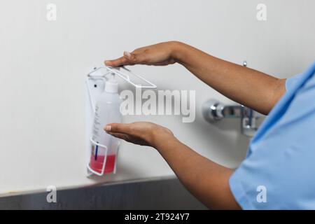 Mittelteil einer birassischen Ärztin mit Peelings, die im Operationssaal Hände waschen Stockfoto