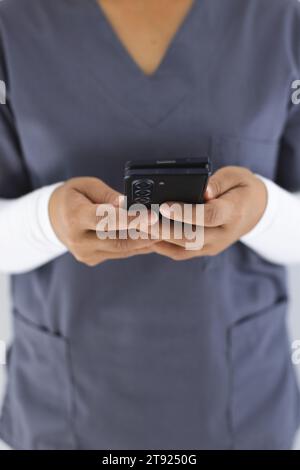 Mittelschnitt einer birassischen Ärztin mit Smartphon im Krankenhaus Stockfoto