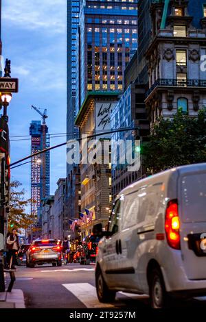 Verkehr in Manhattan, New York City in der Abenddämmerung mit Autos, die am Abend im Herbst durch eine Kreuzung unter Wolkenkratzern in Midtown fahren Stockfoto