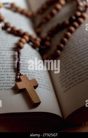 Rosenkranz mit einem hölzernen christlichen Kreuz auf einer Bibel mit offenen Seiten Stockfoto