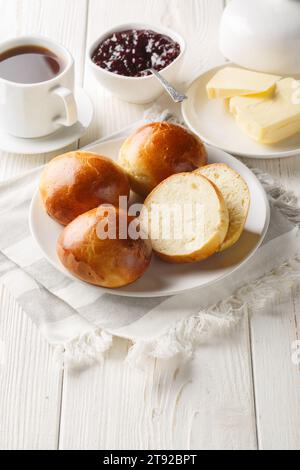 Norwegische Kardamombrötchen mit Butter, Marmelade und Kaffee auf dem Holztisch. Vertikal Stockfoto