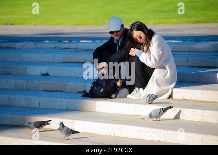 Ein junges Paar sitzt auf der Treppe und füttert Tauben im Park. Stockfoto