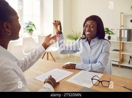 Ein lächelnder afroamerikanischer Immobilienmakler oder Immobilienmakler gibt ihrem glücklichen Klienten Hausschlüssel Stockfoto