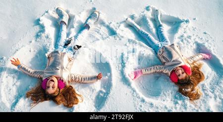 Winterengel. Glückliche Kinder Mädchen auf machen Schnee Engel Flügel. Zwei Kinder machen Schneeengel, liegen auf Schnee. Aufgeregt Kind spielt auf Winter Hintergrund Stockfoto