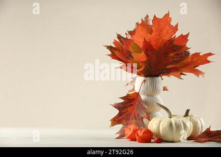 Schöne Herbstblätter in Vase, Kürbisse und Physalis auf dem Tisch vor beigem Hintergrund, Platz für Text Stockfoto