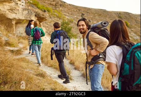 Porträt eines lächelnden männlichen Wanderers mit Rucksack, der mit seinen anderen Wanderern zum Gipfel des Berges geht. Stockfoto