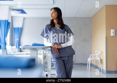 Birassische Ärztin, die aus dem Fenster im sonnigen Krankenhauszimmer schaut Stockfoto