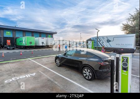 Das Bild zeigt eine Allego-Ladestation, wo ein Tesla und einige Voltazero Elektrofahrzeuge geparkt sind und einige Arbeiter und Kegel auf der Straße sind Stockfoto