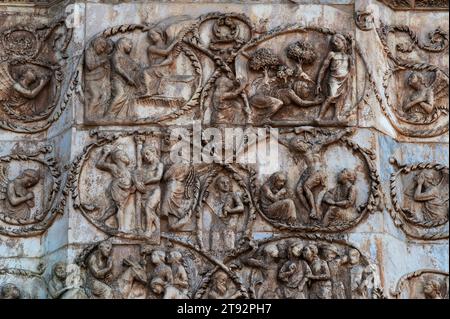 Teil der Marmorplatte mit Basreliefen, die Szenen aus dem Neuen Testament und dem Leben von Maria und Jesus an der Westfront der Kathedrale in Orvieto, Umbrien, Italien, im Duomo di Santa Maria Assunta darstellt. Die Skulptur, die die Westfront bereichert, wurde von einem Team unter der Leitung des italienischen Architekten und Bildhauers Lorenzo Maitani (ca. 1275–1330) ausgeführt. Die Szenen in diesem Detail umfassen Judas’ Verrat an Christus mit einem Kuss (unten rechts), die Geißel Christi und die Kreuzigung. Stockfoto