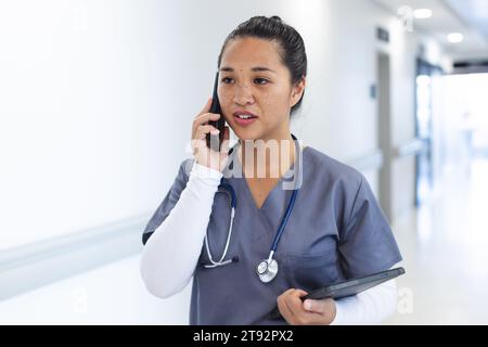 Birassische Ärztin mit Peelings, die auf Smartphone im Krankenhauskorridor sprechen Stockfoto
