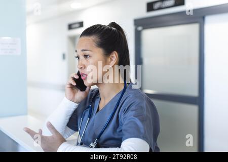 Birassische Ärztin, die am Smartphone an der Rezeption im Krankenhaus spricht Stockfoto