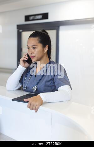 Birassische Ärztin, die am Smartphone an der Rezeption im Krankenhaus spricht Stockfoto