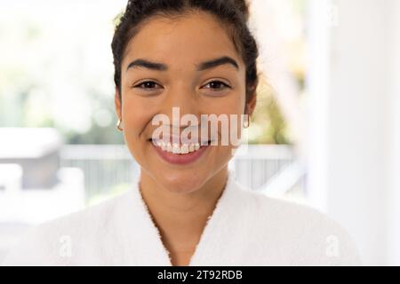 Porträt glücklicher birassischer Frau im Bademantel im sonnigen Bad. Lebensstil, Selbstversorgung und häusliches Leben unverändert. Stockfoto