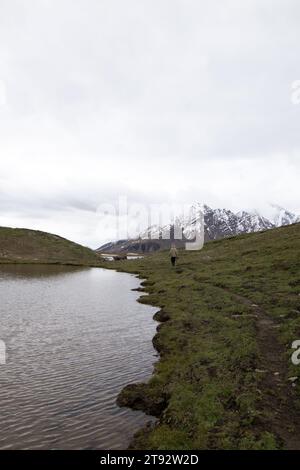 Der Pensila-See, umgeben von schneebedeckten Gipfeln, enthüllt einen ruhigen Himmel. Wildblumen zieren Wiesen und spiegeln die Harmonie der Natur im ruhigen Wasser wider. Stockfoto