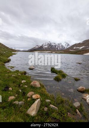 Der Pensila-See, umgeben von schneebedeckten Gipfeln, enthüllt einen ruhigen Himmel. Wildblumen zieren Wiesen und spiegeln die Harmonie der Natur im ruhigen Wasser wider. Stockfoto