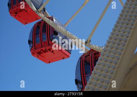 Nahaufnahme der roten Riesenrad-Gondelwagen auf dem Tourist Wheel Fremantle, die tagsüber vor einem blauen Himmel mit einer Reihe von Glühbirnen gesehen werden Stockfoto