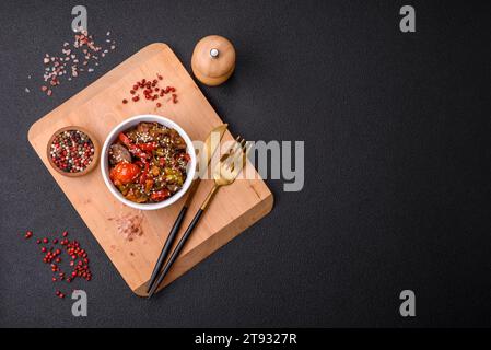 Warmer Salat mit Kalb, Tomaten, Paprika, Zucchini, Sesam, Salz, Gewürze und Kräuter auf dunklem Betonhintergrund Stockfoto