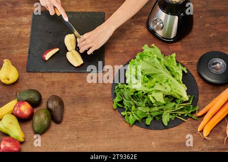 Zugeschnittene Ansicht einer Frau, die Apfel in der Nähe von Elektromixer und Salat mit Minze, pflanzlicher Ernährung schneidet Stockfoto