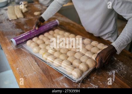 Porträt einer Vielzahl kleiner Teigkugeln auf einem Tablett auf einem Tisch, während ein Bäcker sie in einer Bäckerei mit Plastik bedeckt Stockfoto