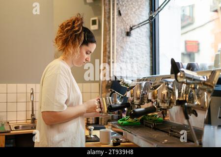 Junger Barista in legeren Kleidern, der Milch aufschäumt, um in einem modernen Café Kaffee zu kochen Stockfoto