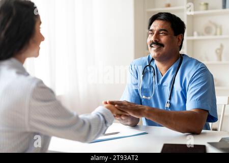 Lächelnder reifer indischer Arzt, der die Hand einer Patientin im Amt hält Stockfoto