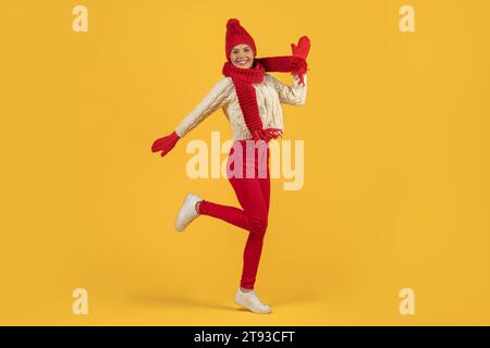 Fröhliche Frau in rotem Strickmütze, die auf gelbem Hintergrund springt Stockfoto