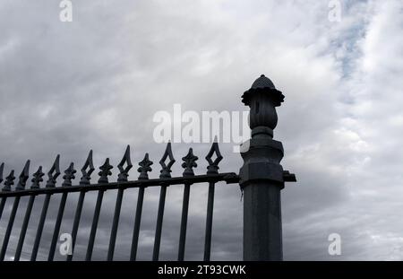 Schmiedeeisernes Tor dekorative Zaunpfosten oben vor dunklem stürmischen Hintergrund Himmel Stockfoto