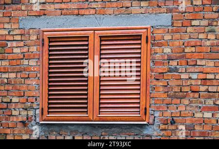 Fenster und Fensterläden an einer roten Backsteinmauer. Holzfenster mit Rollläden, außen isoliert. Außenläden aus braunem Holz. Außenläden. Stockfoto