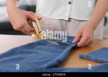 Frau macht zerrissene Jeans am Holztisch, Nahaufnahme Stockfoto