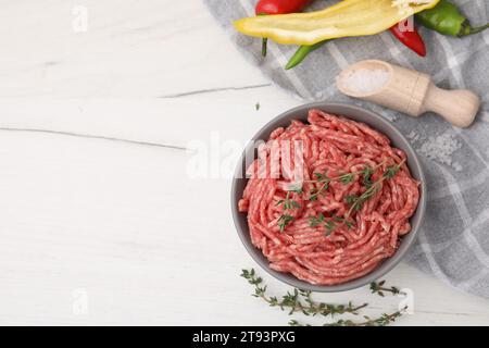 Flache Lagenkomposition mit frischem rohem Hackfleisch und Thymian in Schüssel auf weißem Holztisch. Leerzeichen für Text Stockfoto