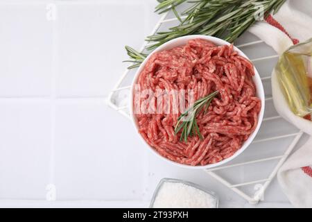 Flache Lagenkomposition mit frischem rohem Hackfleisch und Rosmarin in Schüssel auf weißem Fliesentisch. Leerzeichen für Text Stockfoto