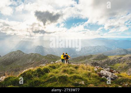 Ein paar Wanderer mit Rucksäcken, die auf einem Berg stehen und umarmen und die Landschaft der Bergkette betrachten. Sport und Outdoor Stockfoto