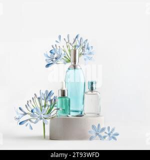 Schönheitsprodukte in blauen Glas-Spray- und Pipettenflaschen, die auf dem Podium stehen, mit Blumen und Blütenblättern auf weißem Hintergrund. Kosmetische Einstellung mit Serum, pe Stockfoto