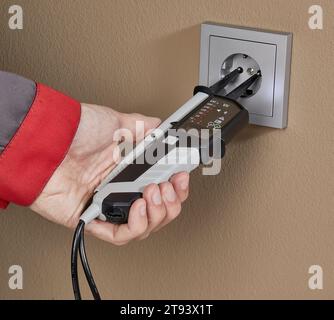 Elektriker, der die Spannung in der Steckdose mit einem professionellen Digitalmultimeter einhändig misst. Stockfoto