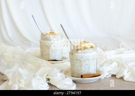 Chiasamen aus der Salvia hispanica Pflanze. Glasbecher, der die Samen enthält, die mit natürlichem Joghurt, Haferflocken, Leinsamen und Banane hydriert sind, Stockfoto