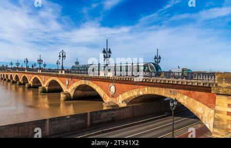 Eine Straßenbahn, die über die Steinbrücke über die Garonne in Bordeaux in Gironde, Nouvelle-Aquitaine, Frankreich, fährt Stockfoto