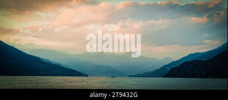 Malerischer Blick auf den wunderschönen Comer See in Italien, umgeben von Bergen, die von farbenfrohen Häusern gesäumt sind und mit Bäumen bedeckt sind, die ihre Farbe ändern Stockfoto